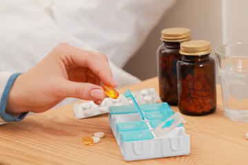 Woman taking pill from plastic box at wooden table, closeup