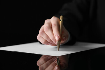 Woman writing on sheet of paper at glass table, closeup