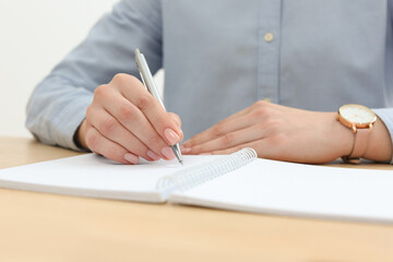 Woman writing in notebook at wooden table, closeup