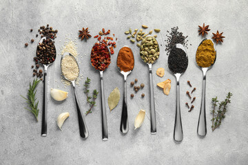 Metal spoons with different spices on light grey table, flat lay