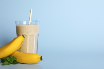 Glass of tasty smoothie with straw, bananas and mint leaves on light blue background. Space for text