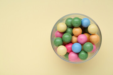Fototapeta na wymiar Bowl with many bright gumballs on beige background, top view. Space for text