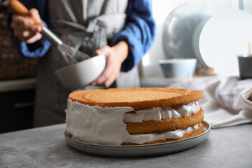 Woman decorating delicious homemade layer cake with cream at grey table, closeup