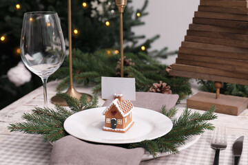 Festive place setting with beautiful dishware, cutlery and gingerbread house card holder for Christmas dinner on white wooden table