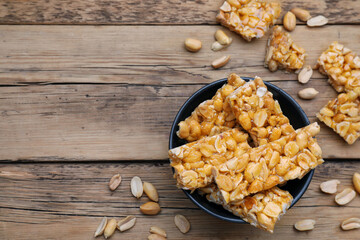 Delicious peanut kozinaki bars in bowl on wooden table, flat lay. Space for text