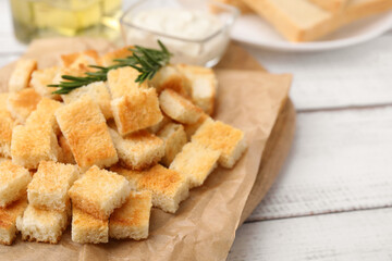Delicious crispy croutons with rosemary on white wooden table, closeup