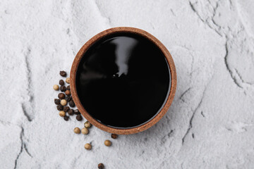 Wooden bowl with balsamic vinegar and peppercorns on white textured table, top view