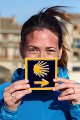 Young beautiful female pilgrim's portrait posing with the typical "Camino de Santiago" blue  tile painted with a yellow shell and arrow.