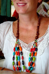 Close up of a wooden necklace worn by a cheerful young woman sitting in a cool restaurant in Puerto Viejo, Costa Rica.