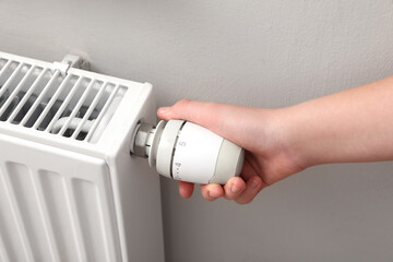 Girl adjusting heating radiator thermostat near white wall, closeup