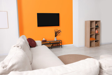 Stylish sofa and wooden furniture near orange wall in spacious room. Interior design