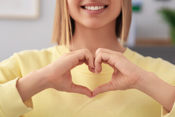 Young woman making heart with hands indoors, closeup. Volunteer concept