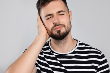 Obraz premium Young man suffering from ear pain on light grey background