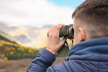 Boy looking through binoculars in beautiful mountains, closeup. Space for text