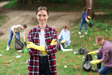 Young woman in gloves and group of people collecting garbage outdoors