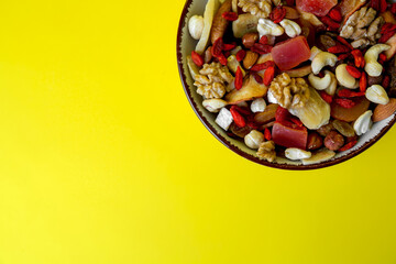 Bowl with mixed dried fruits and nuts on yellow background, top view. Space for text