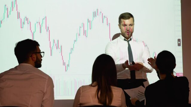 Trader presents stock market investment strategy for group of investors on candlestick chart. Speaker is discussing with participants in the meeting of the prospect of growth or falling stock market