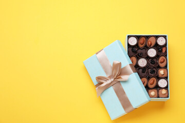 Open box of delicious chocolate candies on yellow background, flat lay. Space for text