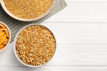 Bowls with dried orange seasoning zest and peel on white wooden table, flat lay. Space for text