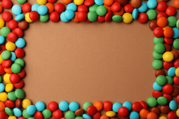 Frame of tasty colorful candies on light brown background, flat lay. Space for text