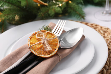 Festive place setting with beautiful dishware, fabric napkin and dried orange slice for Christmas dinner on white table, closeup