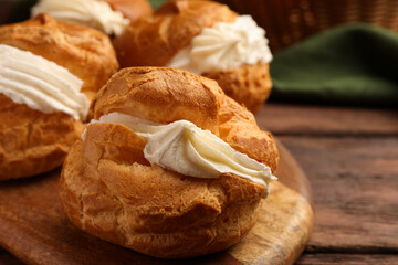 Delicious profiteroles with cream filling on wooden table, closeup