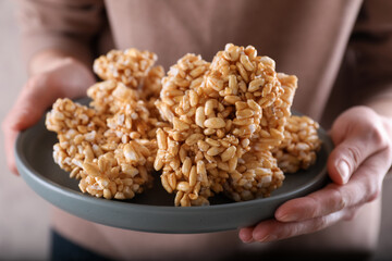 Woman holding plate with puffed rice pieces (kozinaki), closeup