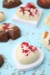 Tasty chocolate heart shaped candies with nuts on light blue background