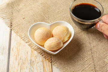 cheese bread in heart shaped container on wooden table with cup of coffee, coffe break morning meal concept with traditional brazilian food