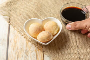 cheese bread in heart shaped container on wooden table with cup of coffee, coffe break morning meal concept with traditional brazilian food