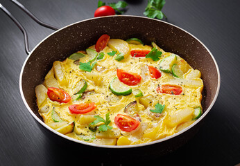 Omelette with tomatoes,  zucchini and potatoes on dark background. Healthy diet food for breakfast. Tasty morning food.