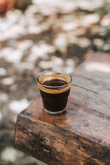 Hot sturdy Americano in a glass glass on a wooden countertop. Black coffee on a walk. Stylish photo to advertise coffee with space for text. A minute of coffee break