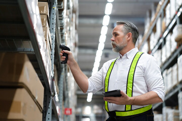 Senior warehouse manager scan boxes by using scanner to count inventory balance in online system, holding tablet in hand for checking real time update. Logistic, warehouse, inventory concept.