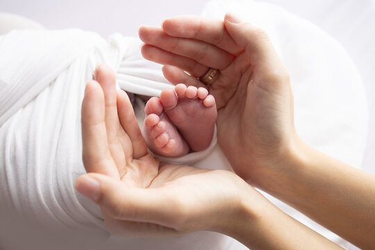 Small feet of a newborn in the hands of a parent. Loving palms of mother's hands. Conceptual image of motherhood. Close-up, selective focus. Professional photography on a white background.