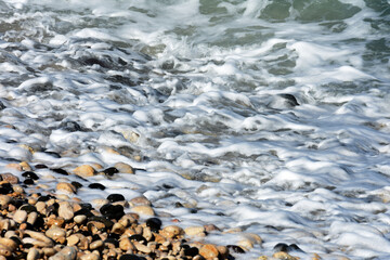 Texture of pebbles on the beach with white waves crashing