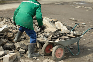 Worker collects stones in cart. Construction debris in garden cart.