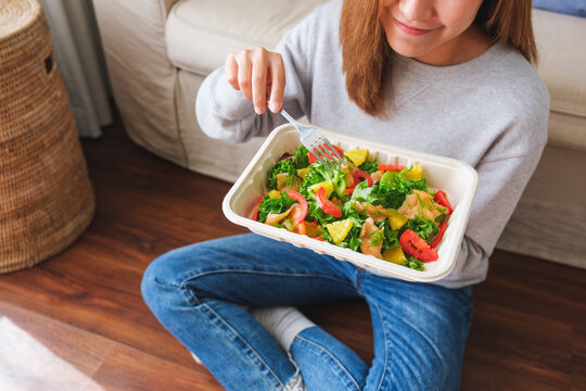 Closeup image of a young woman eating salad in paper box for takeaway food at home