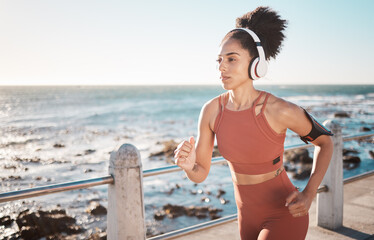 Black woman, fitness and running with headphones at the beach on sea point in Cape Town for...