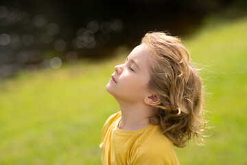Child breathing fresh air. Child faith, praise and happiness and freedom. Kid resting in summer park. Kid put face to the sun, closed her eyes and feeds energy of nature, dreams. - obrazy, fototapety, plakaty