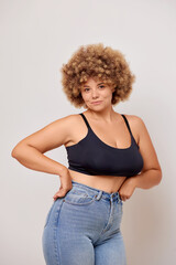Confident plus size woman with Afro hair feels confident, wears jeans and black lingerie bra, poses...