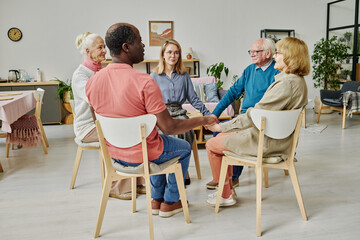 Elder people getting support at psychotherapy session, they sitting in circle and holding hands