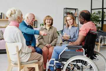 Group of senior people sitting in circle and talking to caregiver in nursing home during therapy - obrazy, fototapety, plakaty