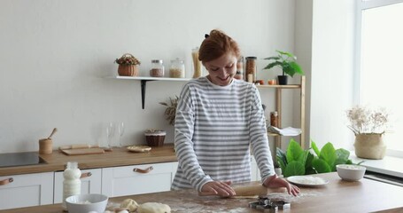 Young redhead woman hold rolling-pin flatten handmade dough cooking alone in kitchen, prepare surprise for family on holidays. Culinary, portrait of happy housewife engaged in everyday routine at home