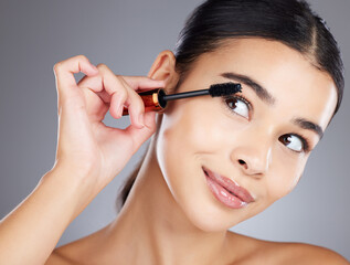 Beauty makeup, face and woman with mascara in studio isolated on gray background. Cosmetics, thinking and closeup of young female model with brush, tool or product for care of eyelashes for wellness.