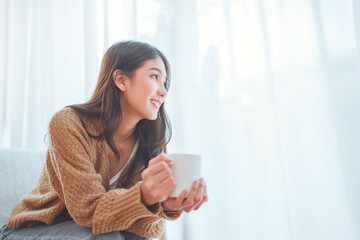 Happy asian woman relaxing drinking hot coffee or tea in holiday morning vacation on armchair at...