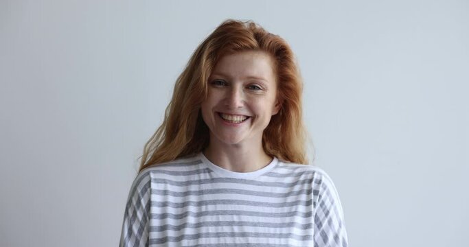 Head shot beautiful happy smiling red-head woman in casual striped shirt pose on gray studio wall background, staring at camera, feels satisfied. Millennial generation person portrait, natural beauty