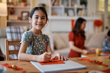 Happy Asian girl writing Chinese couplets with ink at home and looking at camera.