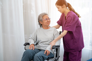 Asian young nurse taking care and talking mature female patient sitting on wheelchair in hospital. Healthcare concept.