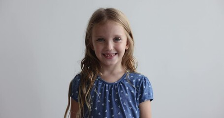 Cute blonde preschooler girl in casual blue printed shirt smile revealing erupted teeth, staring at camera while pose alone on gray studio wall background. Alpha generation child, head shot portrait