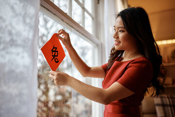 Happy Chinese woman decorating window with calligraphy for Lunar New Year celebration.